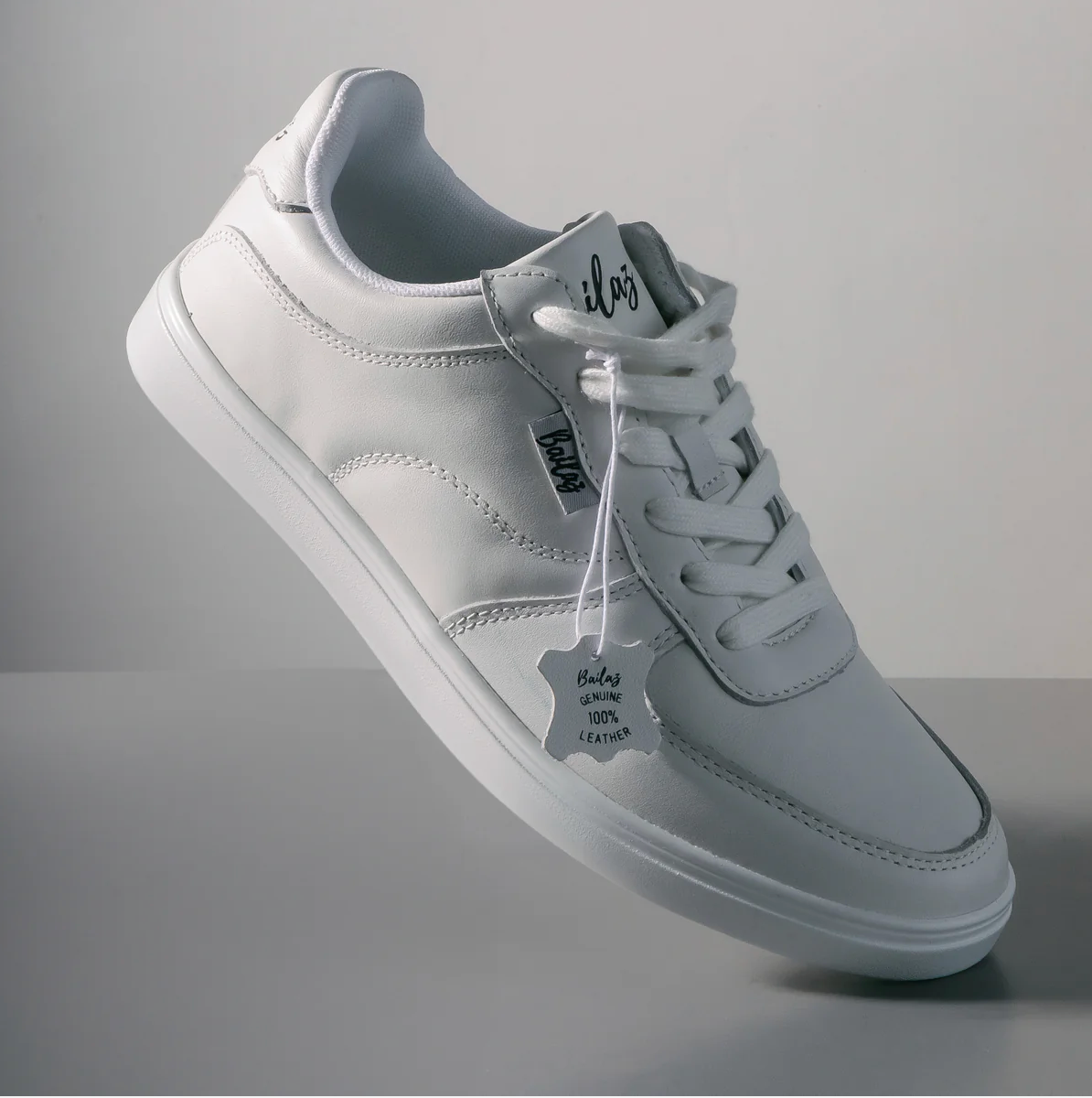 Close-up of a white dance shoe with the brand name 'Bailaz' on the lace tag, featuring a genuine leather upper and a proprietary polyurethane composite outsole - Angled View
