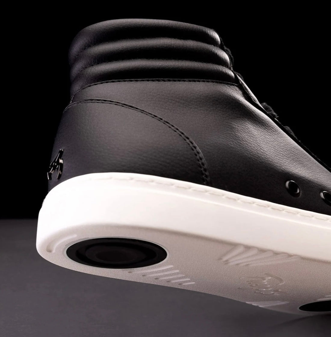 A black high-top sneaker with a white sole, showcasing the shoe's side profile with visible breathable air holes and a flame logo. Dual black pivoting disks visiable. 