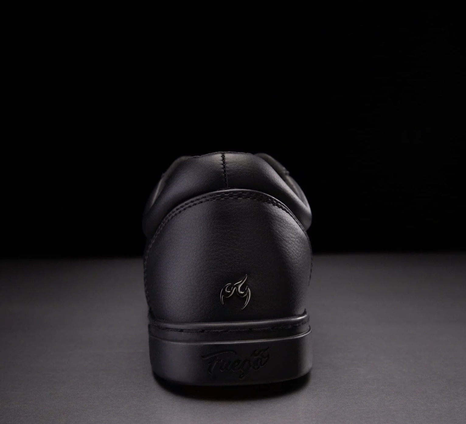 The back of an all black dance shoe. Showcasing their flame logo in black.